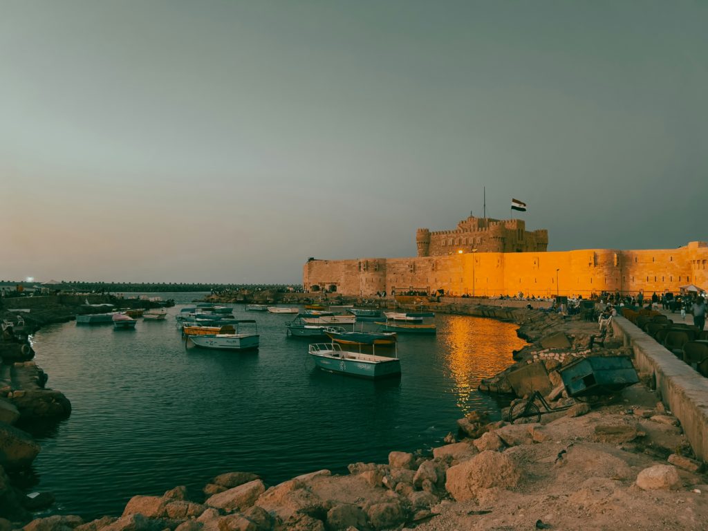 wide shot of alexandria's shoreline with a castle in the background