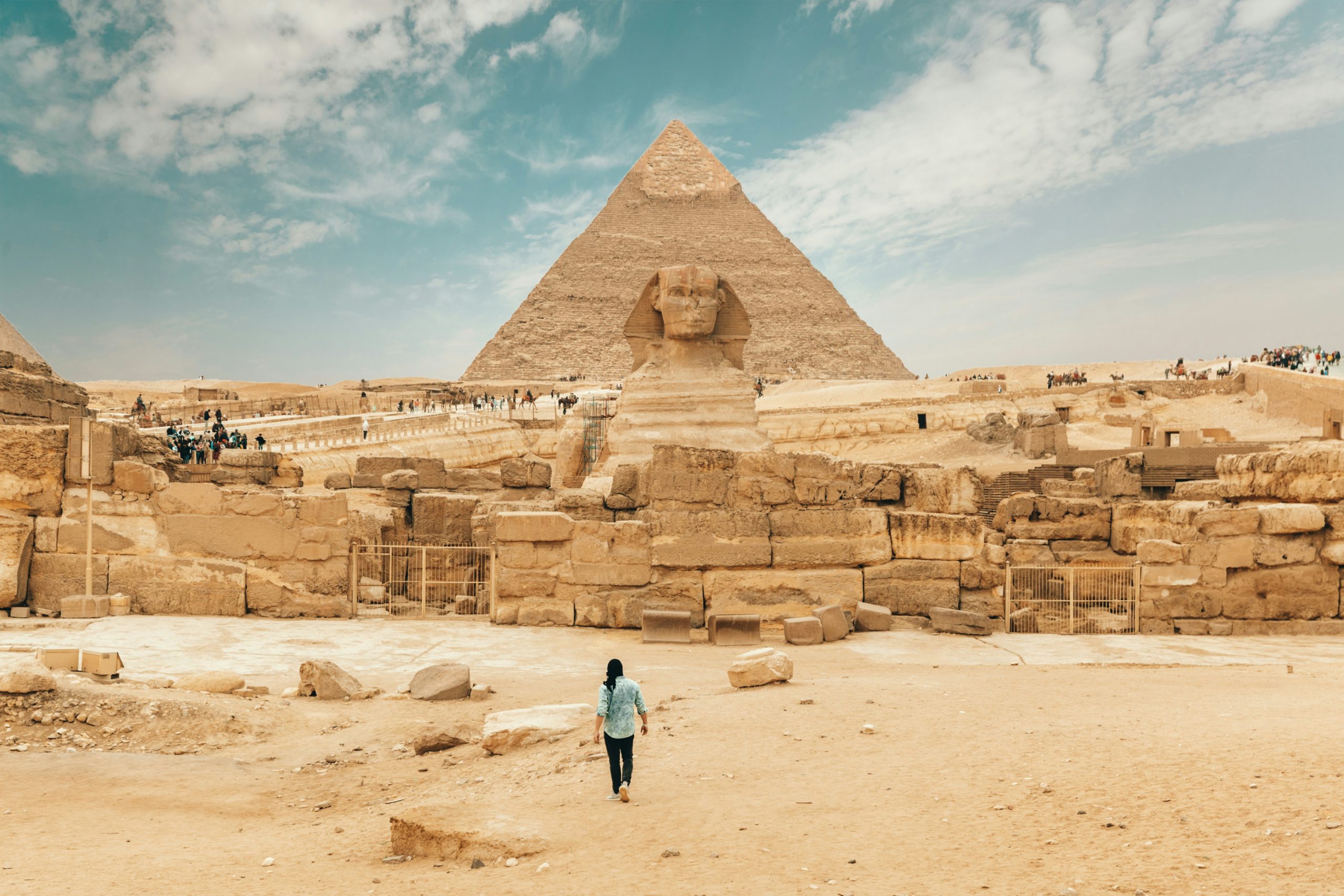 Man walking towards the Sphinx with the Pyramids of Giza behind